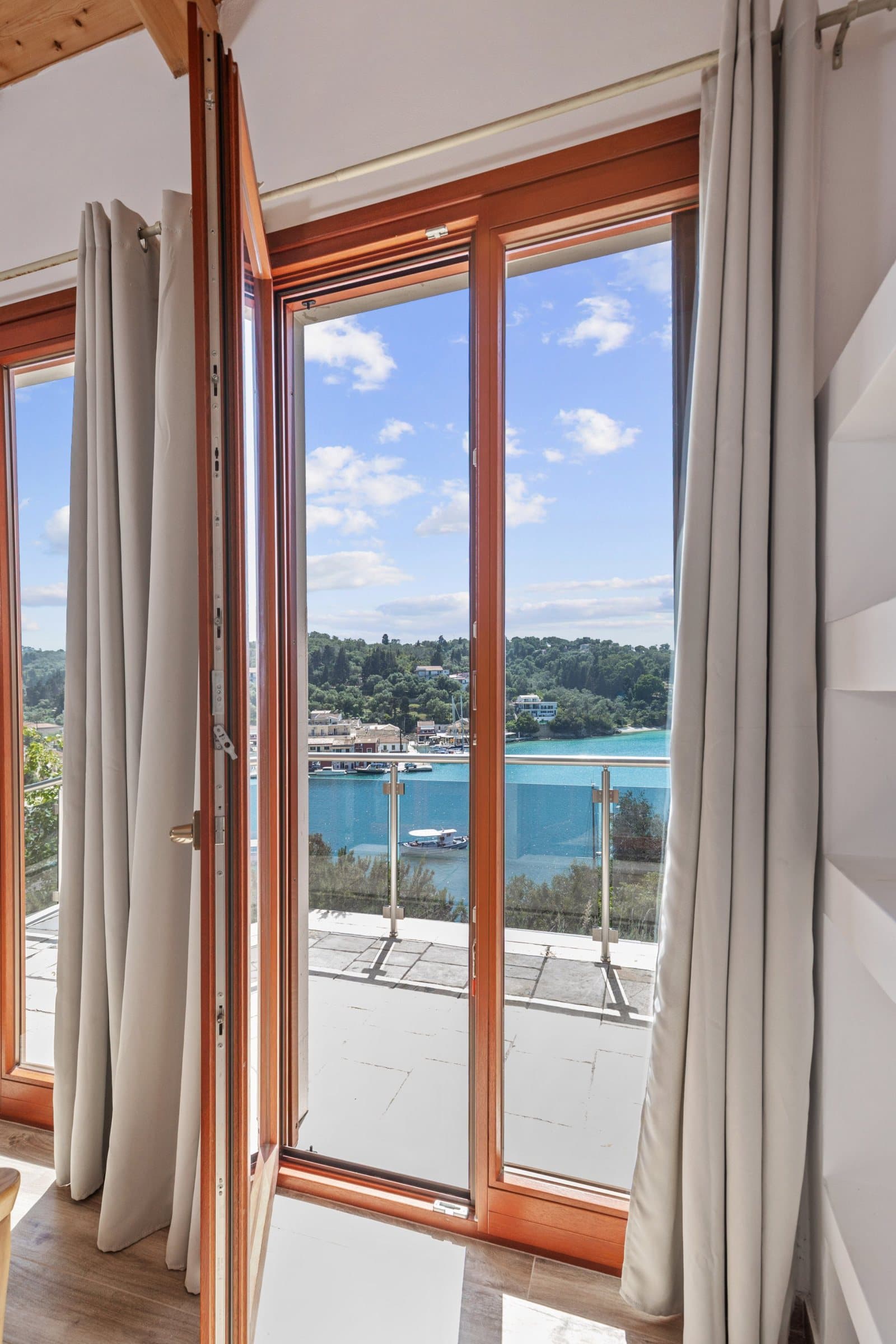 Open French windows with linen curtains looking out over the balcony to Lakka bay