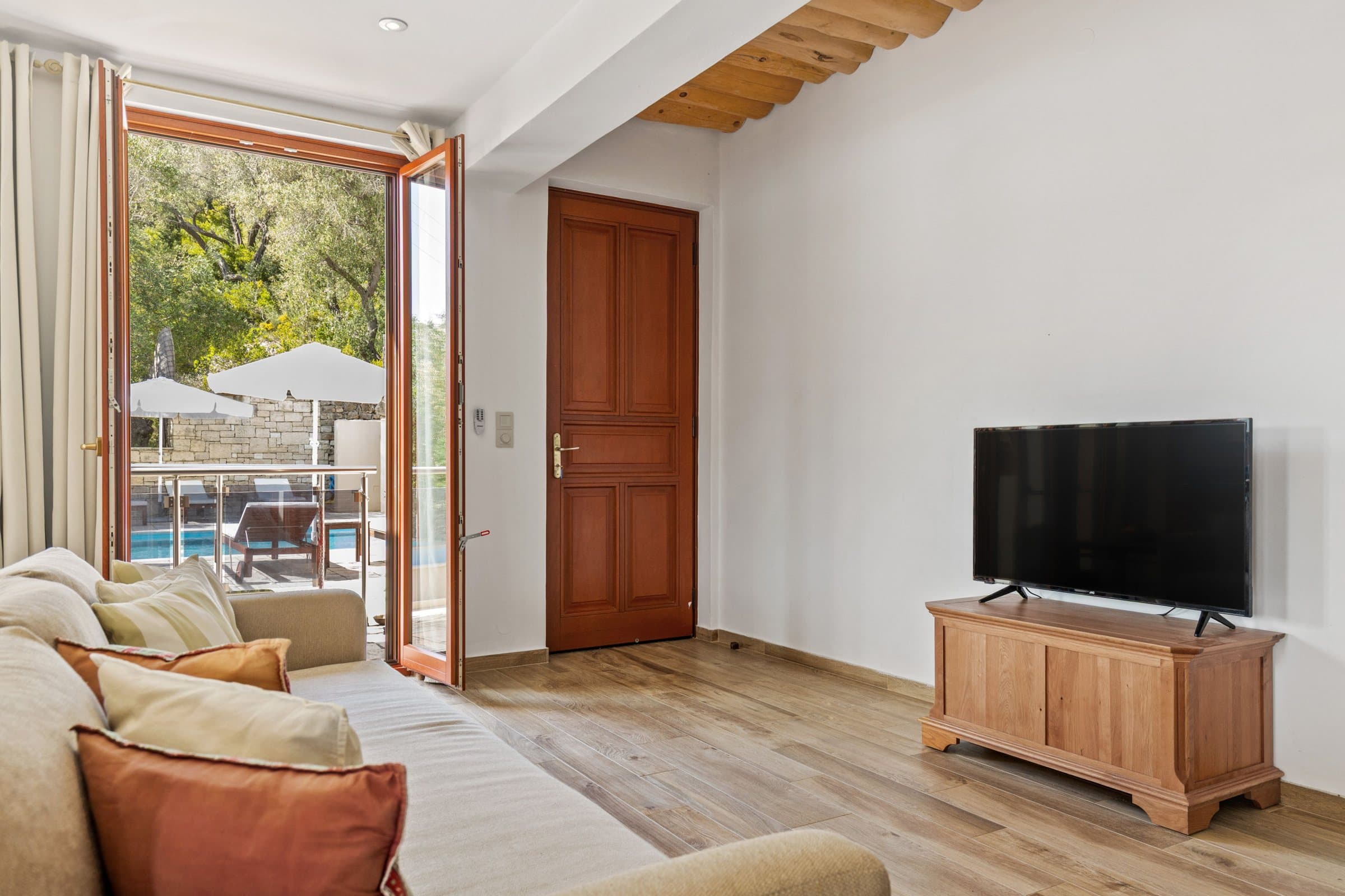 Living room with a cream sofa, terracotta cushions and doors open to the pool terrace