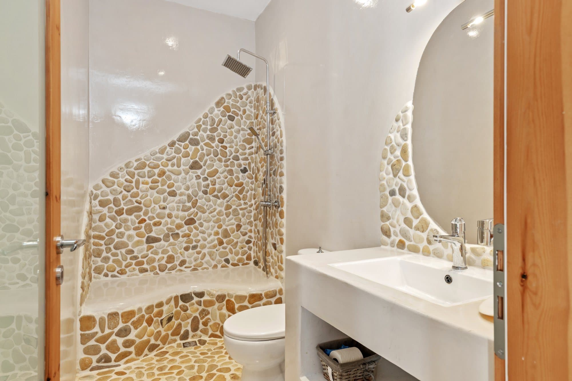 Bathroom with a walk-in shower set in hand-laid pebble walls and a white basin