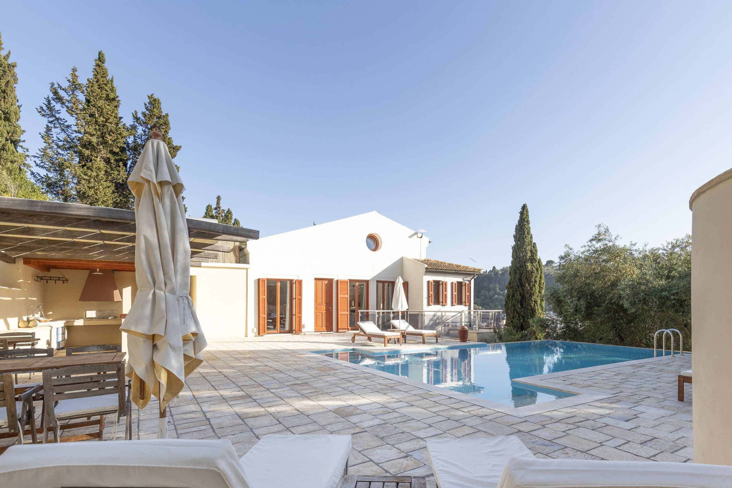 Shaded pergola, parasol and pool terrace looking towards the villa on a sunny day