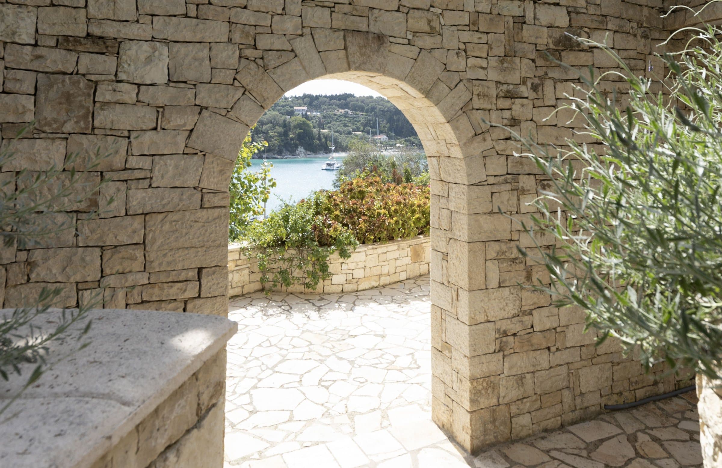 Stone arch in the garden wall framing a glimpse of the sea and the far shore of the bay