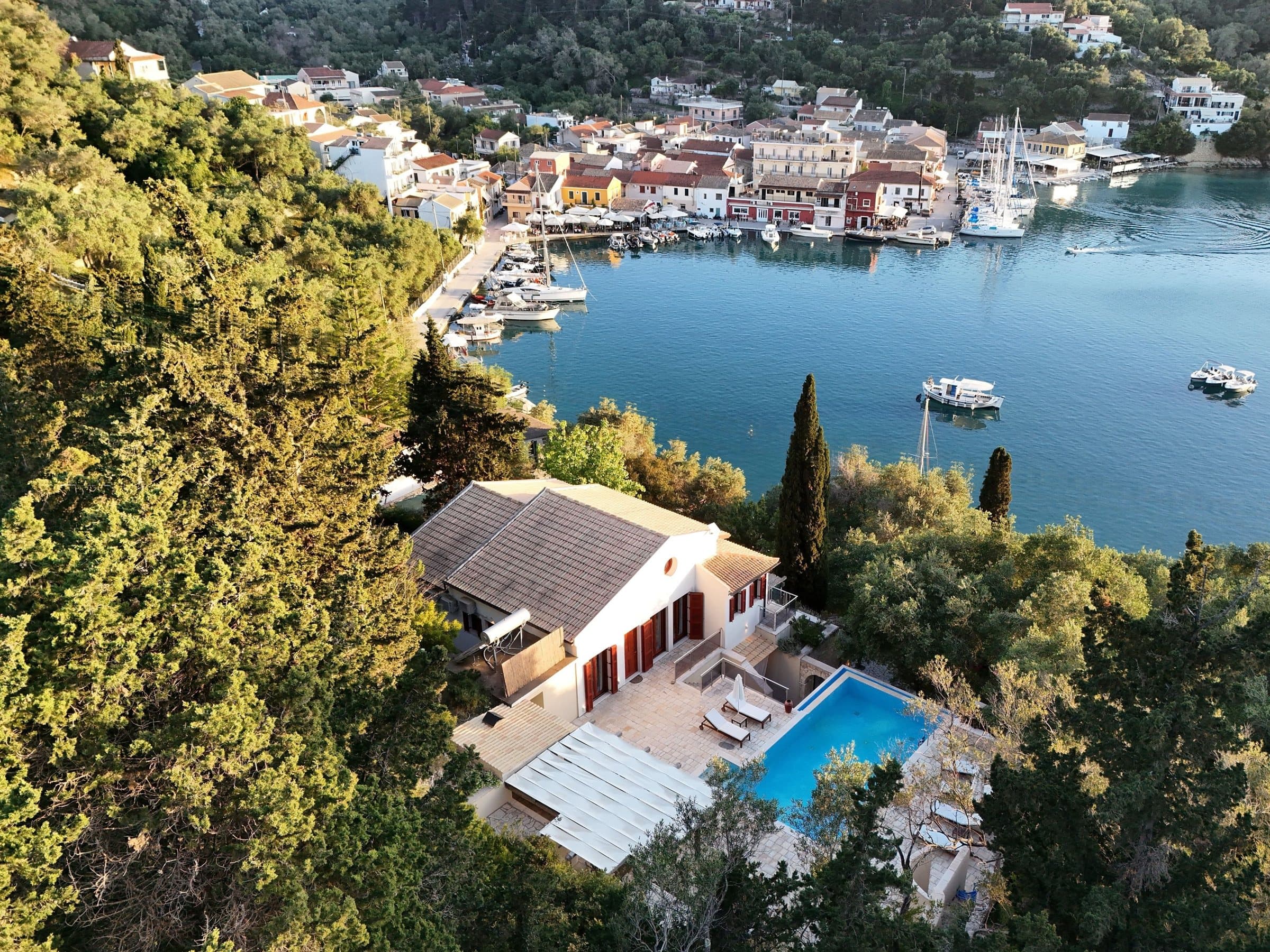 Aerial view of Villa Blotto and its pool on the wooded hillside directly above Lakka bay and village, Paxos
